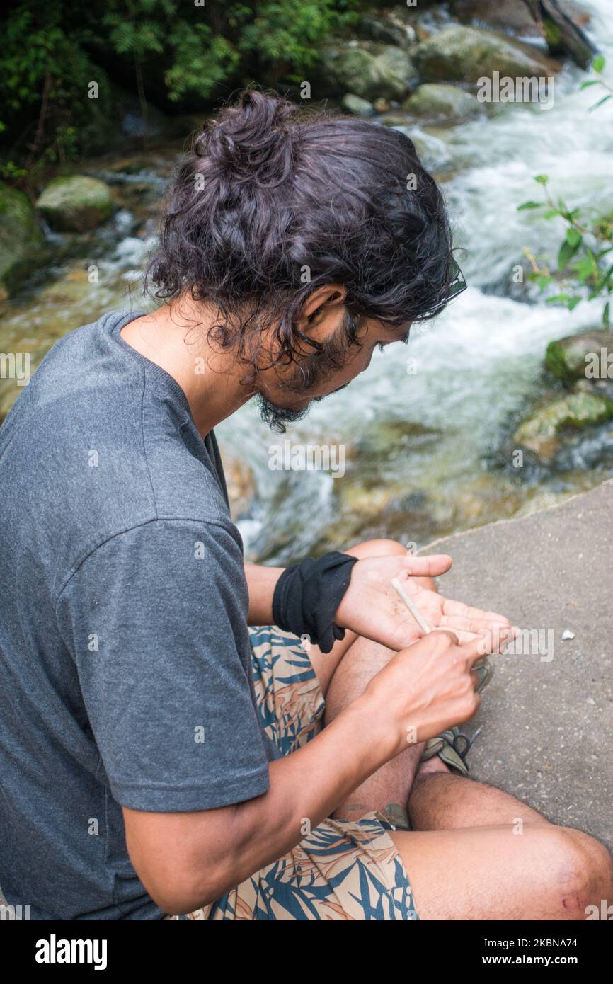 July 14th 2022, Himachal Pradesh India.. A side pose of a young man with a man bun rolling a weed joint in the hills of Himalayas. Stock Photo
