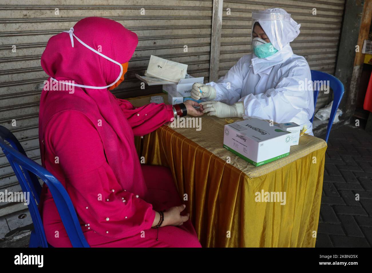 Medical personnel wearing personal protective equipment take blood samples during the Covid-19 rapid test to traditional market traders in Sidoarjo, East Java, on May 6, 2020. The Indonesian government continues to conduct a Covid-19 rapid test on residents to be immediately free of the Covid-19 pandemic. (Photo by Suryanto Putramudji/NurPhoto) Stock Photo