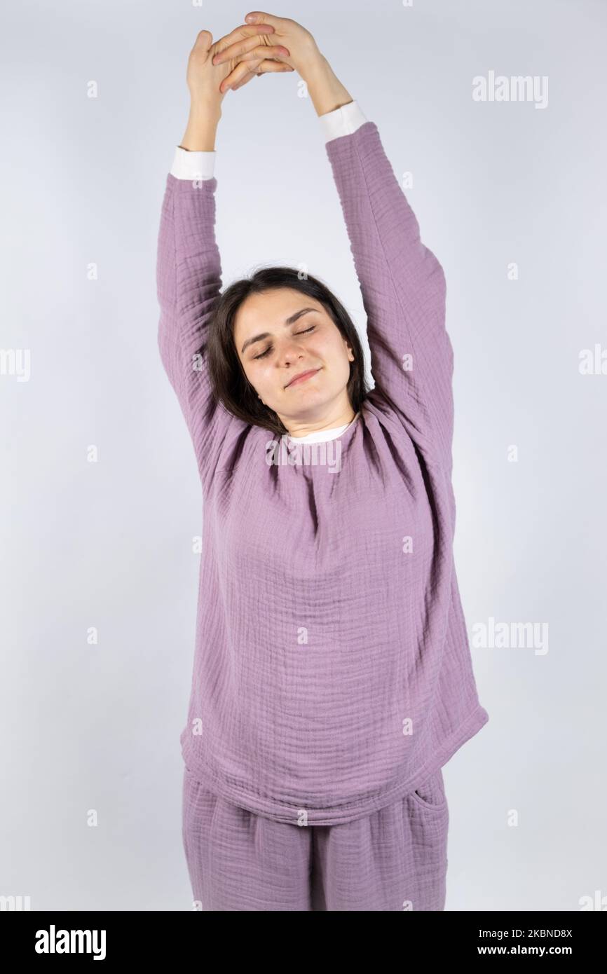 Young woman in muslin lavender pajamas sleep clothes stretches