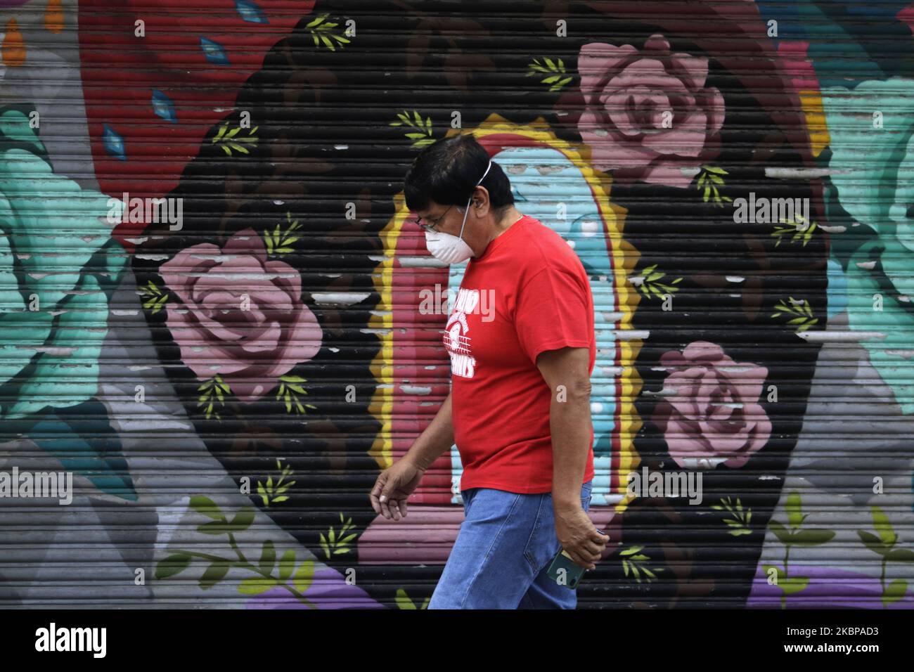 A man in the Zocalo of Mexico City, Mexico, o May 26, 2020 walks in front of a curtain with the image of some roses. The curtains of several businesses in the Historic Center of Mexico City have become protagonists to show the transit of its inhabitants during the Covid-19 health emergency in Mexico. They were intervened with the aim of providing spaces to young people who want to show their artistic skills inspired by various themes such as religion, culture, daily life, entertainment, among others. (Photo by Gerardo Vieyra/NurPhoto) Stock Photo