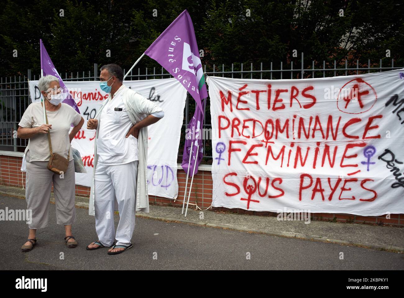 Two protesters stand in front of a banner reading 'Jobs most for females and under paid'. Doctors, nurses and nursing auxiliary gathered in front of the ARS (ie Regional Health Agency) Occitania. Since several months, personnel working in public hospitals demand more means and more people. The Covid-19 pandemic has put french public hospitals at saturation point .They denounce a reduction of people in emergencies services in public hospitals and demand 10 000 nurses more. On June 2, 2020 in Toulouse, France. (Photo by Alain Pitton/NurPhoto) Stock Photo