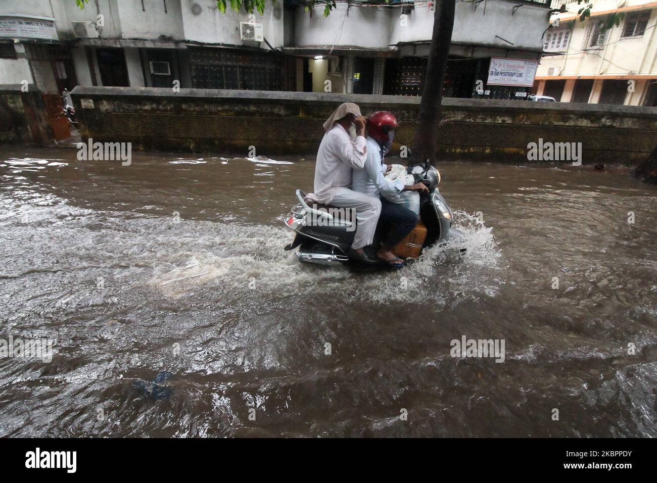People ride a motorcycle through flood waters during heavy rains in