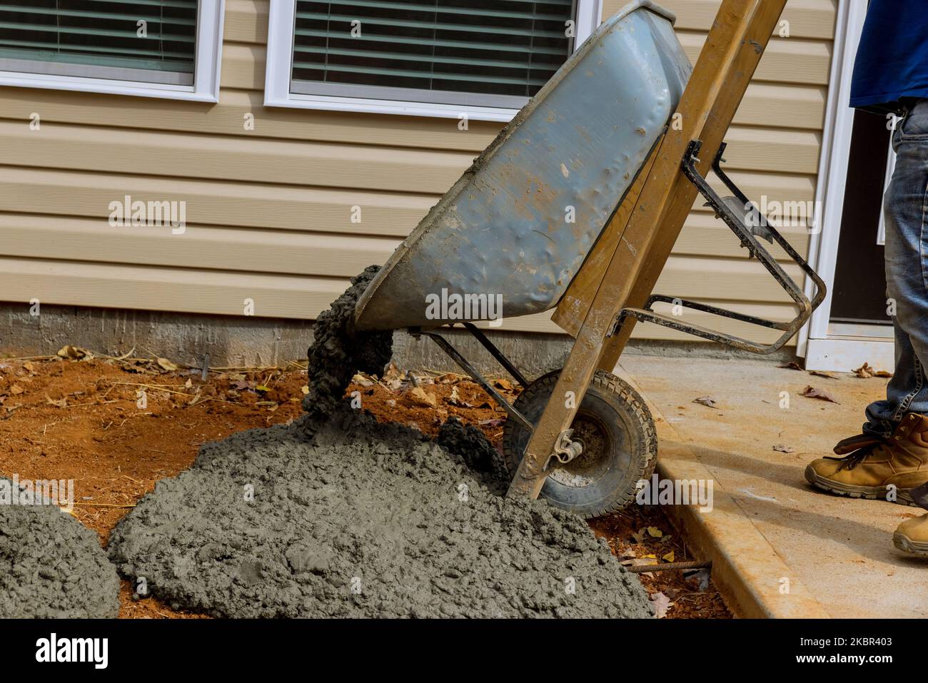 Construction worker pours cement from wheelbarrow on side of home to ...
