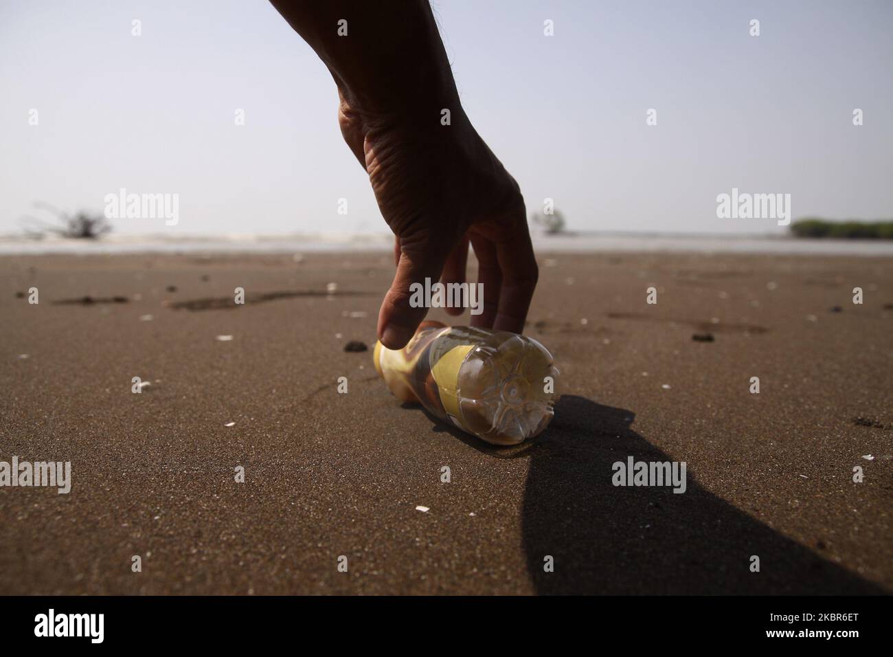 A man picks up the plastic bottle waste left by the tourist on the beach at Pantai Bahagia, Muara Gembong sub-district, Bekasi regency, West Java province, on June 13, 2020. According to the research reports from the Indonesian Institute of Sciences (LIPI), released in 2018, the amount of plastic waste in the Indonesian sea reaches 100.000 - 400.000 tons per year, with an average coastline spread of arround 1.71 pieces per square meter with an average weight of 46.55 grams per square meter. While the highest average plastic waste was found on the coast of Sulawesi, reaching 2.11 pieces per squ Stock Photo