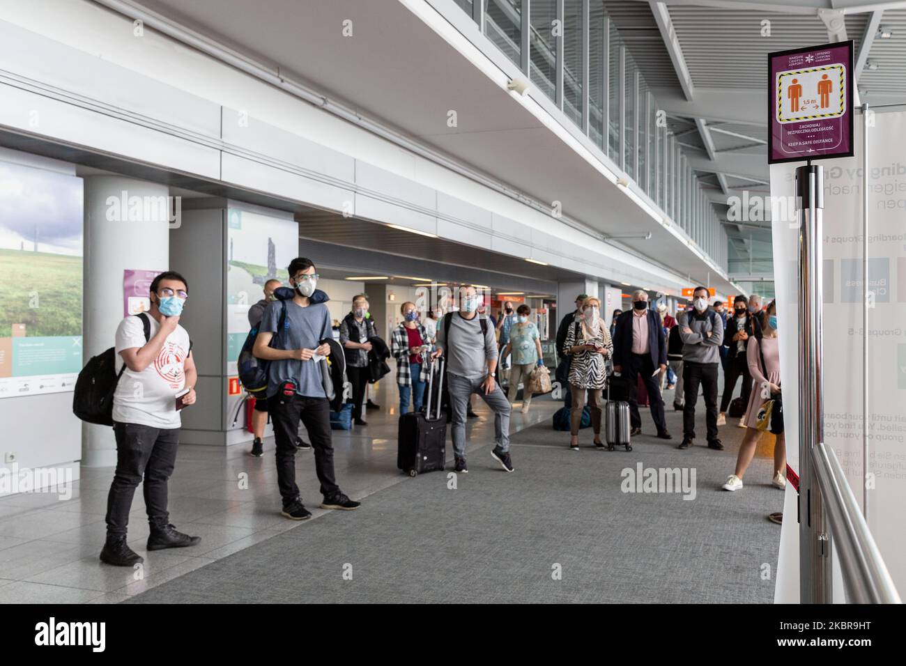 Passengers in protective face masks keep social distance as they wait