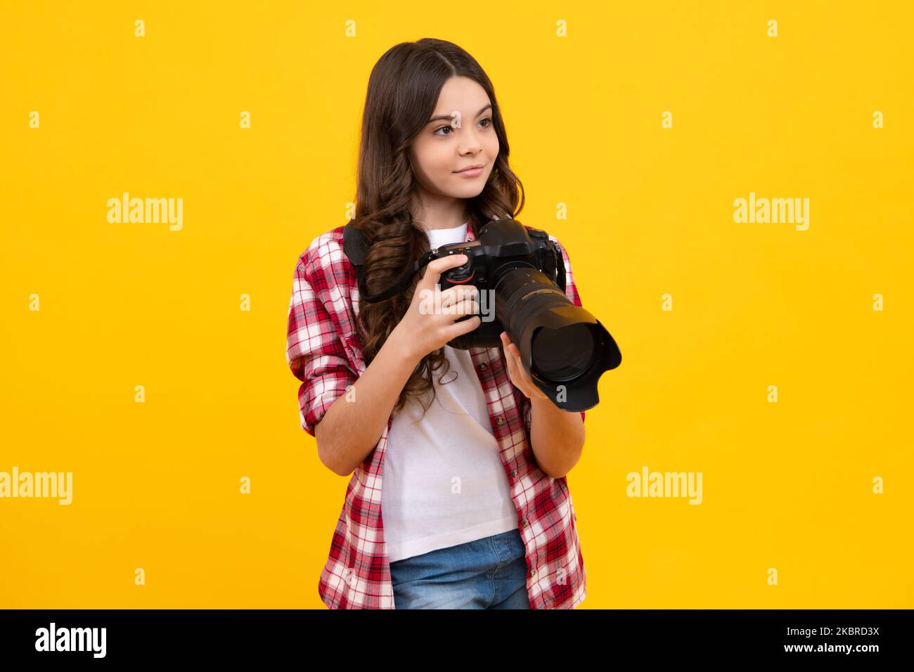 12, 13, 14 year old teen girl holding digital camera or DSLR over yellow background. Stock Photo