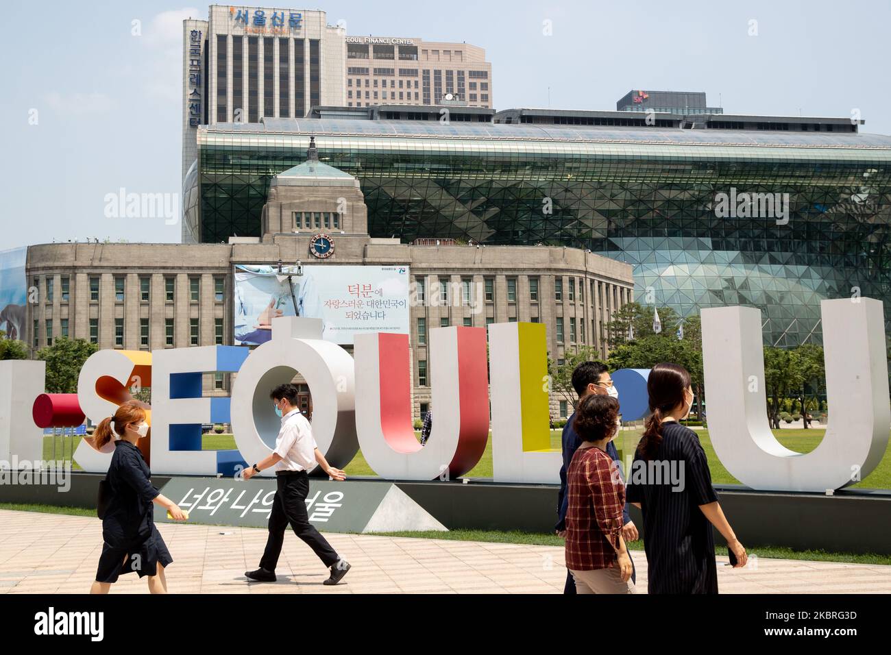 People walk in front of an I SEOUL U billboard, and the City Hall is seen in the background in Seoul, South Korea on June 22, 2020. Today, the temperature in Seoul reach 35 degrees. (Photo by Chris Jung/NurPhoto) Stock Photo