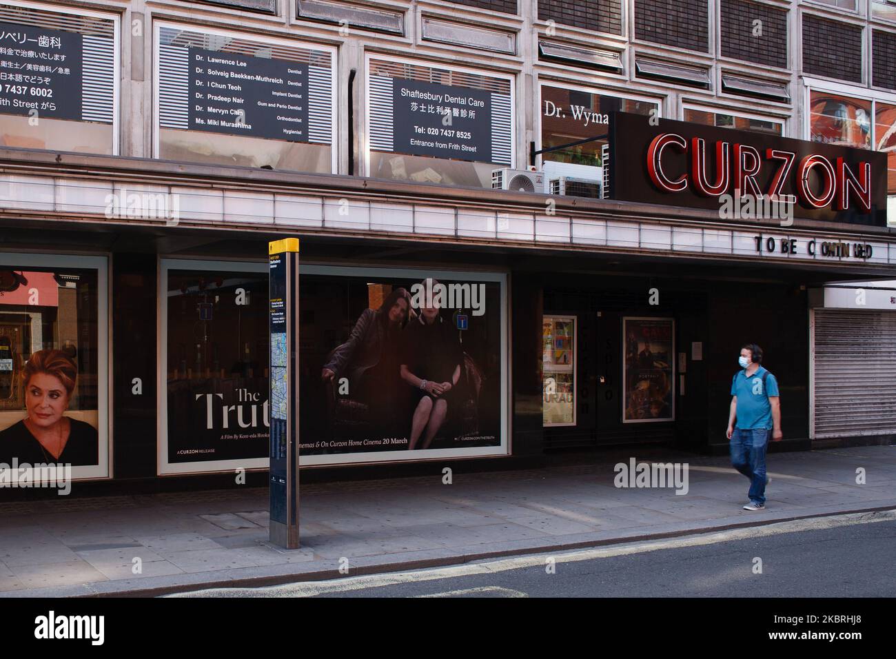 A man wearing a face mask walks past a closed branch of cinema chain Curzon on Shaftesbury Avenue in London, England, on June 23, 2020. British Prime Minister Boris Johnson announced today that the next stage of lockdown easing in England would proceed on schedule, with pubs, restaurants, hotels, hairdressers, theatres, cinemas, museums, galleries, libraries, theme parks and zoos allowed to reopen from July 4. The two-metre social distancing rule is also to be halved from the same date, with people encouraged to take additional mitigation actions, such as wearing face coverings, when close tog Stock Photo
