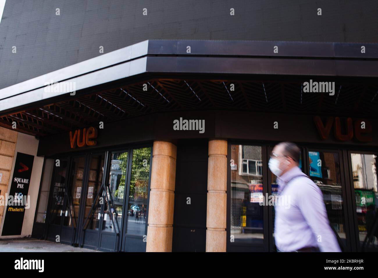 A man wearing a face mask walks past a closed branch of cinema chain Vue in Leicester Square in London, England, on June 23, 2020. British Prime Minister Boris Johnson announced today that the next stage of lockdown easing in England would proceed on schedule, with pubs, restaurants, hotels, hairdressers, theatres, cinemas, museums, galleries, libraries, theme parks and zoos allowed to reopen from July 4. The two-metre social distancing rule is also to be halved from the same date, with people encouraged to take additional mitigation actions, such as wearing face coverings, when close together Stock Photo