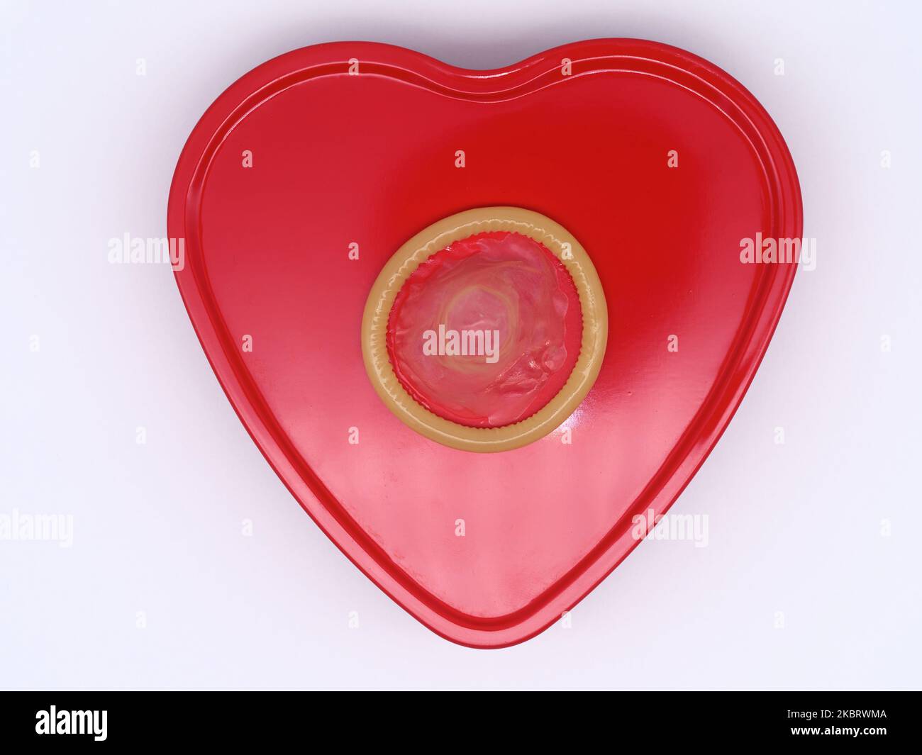 Unwrapped condom on a red heart shape against a white background Stock Photo