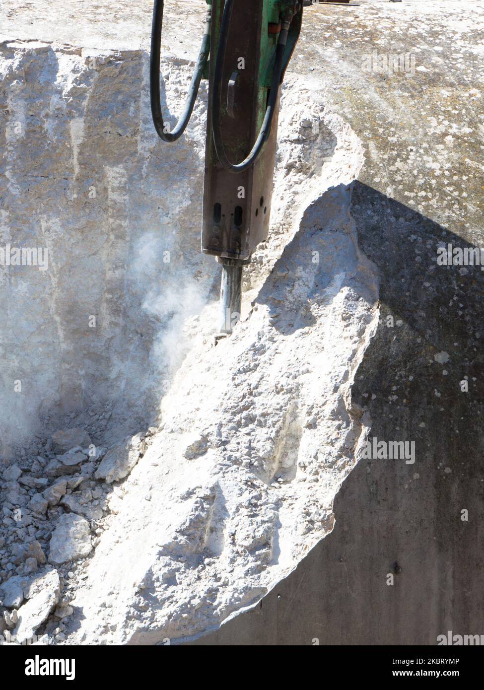Demolishing hard concrete structure with the breaker, percussion hammer mounted on the excavator
