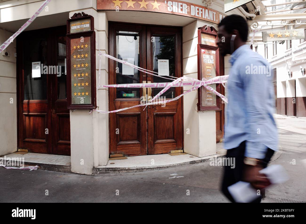 A man walks past tape bearing the message 'Live Theatre Missing' stretched across the entrance to the closed Ambassadors Theatre, previously showing play 'Kunene and the King', on West Street near Cambridge Circus in London, England, on July 6, 2020. The British government last night unveiled a 1.57 billion GBP 'rescue package' for the arts sector, designed to help museums, galleries, theatres, independent cinemas, heritage sites and music venues through the coronavirus pandemic. It follows weeks of lobbying from industry leaders, who have been warning that many venues were on the brink of col Stock Photo