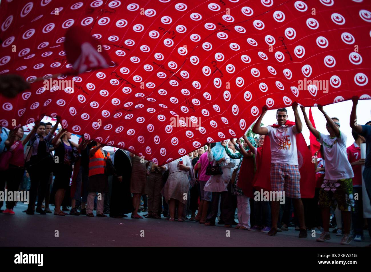 People wave a big tunisien flag during a march outside the National Assembly at the bardo to mark the 40th day since the assassination of opposition politician Mohamed Brahmi. Brahmi was shot dead by unknown gunmen outside his home. On 7 September 2013, in Tunis, Tunisia. (Photo by Emeric Fohlen/NurPhoto) Stock Photo
