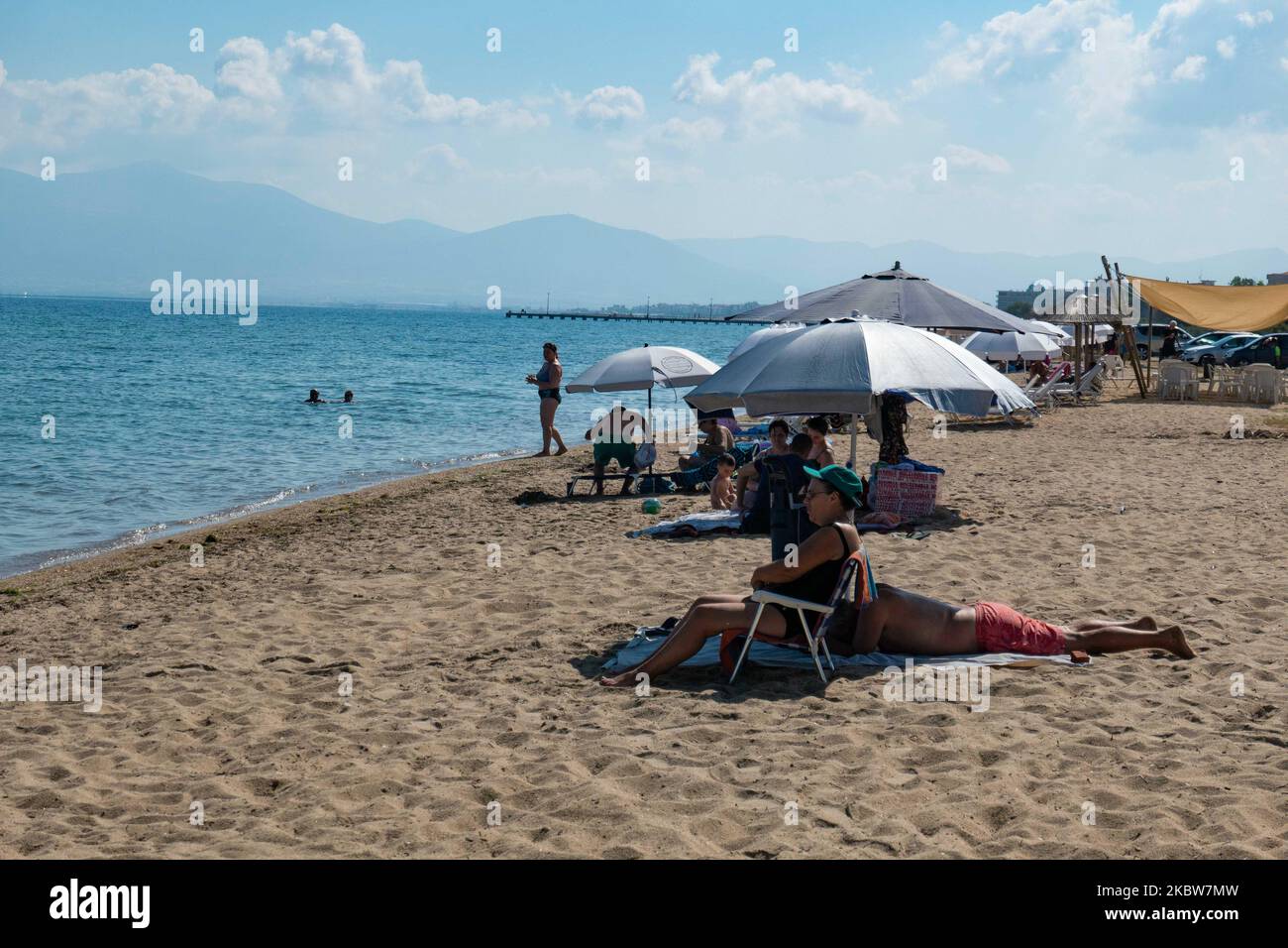 Everyday life at the sandy beach of Agia Triada near Thessaloniki in Greece on July 26, 2020. Agia Triada is a summer tourist destination for locals and foreign tourists for holidays mostly from the Balkan countries. The beach is awarded with Blue Flag, has typical for Greek Beaches and the Aegean Sea, crystal clear transparent sea water, golden sand and many tourism facilities such as a pedestrian waterfront road next to the shore, free showers etc. There are hotels, taverns, restaurants, bars and beach bars in the area, which is just a few minutes driving away from Thessaloniki International Stock Photo