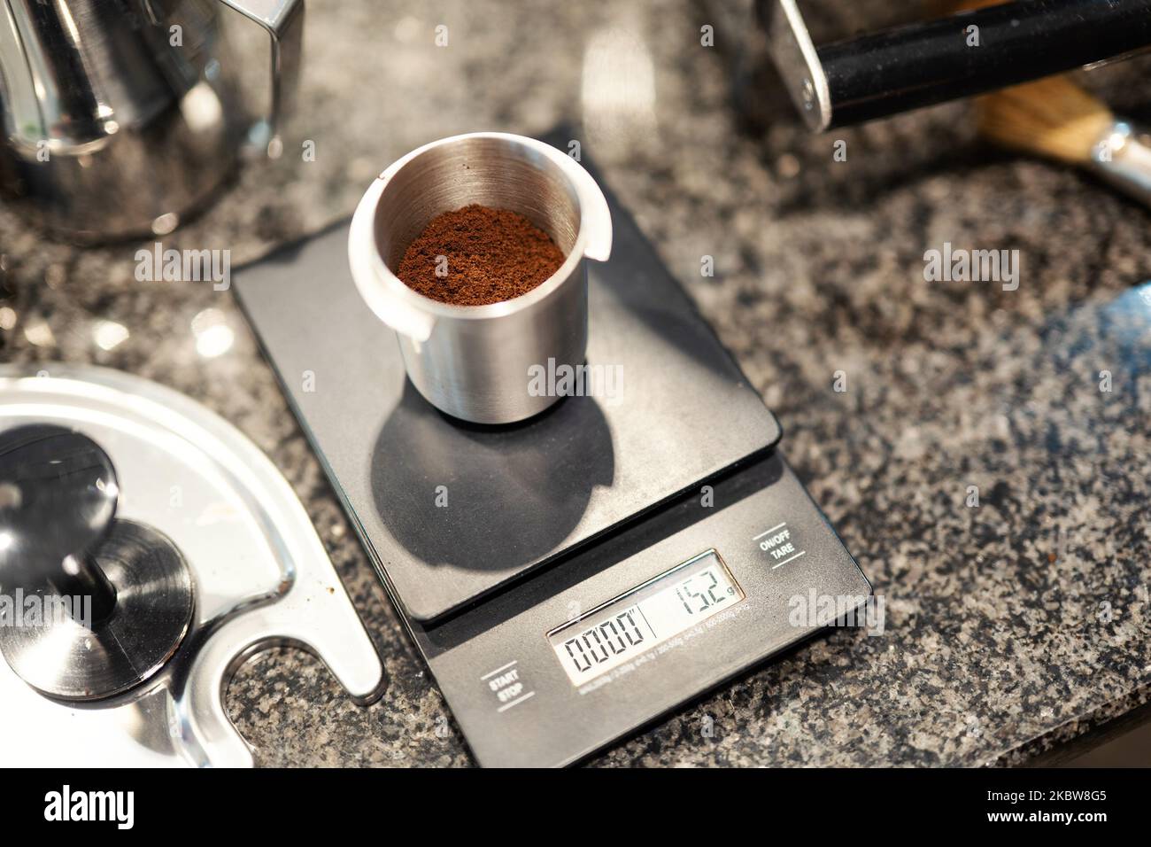 Freshly ground coffee is precisely weighed on a kitchen scale in an aluminum container. Stock Photo
