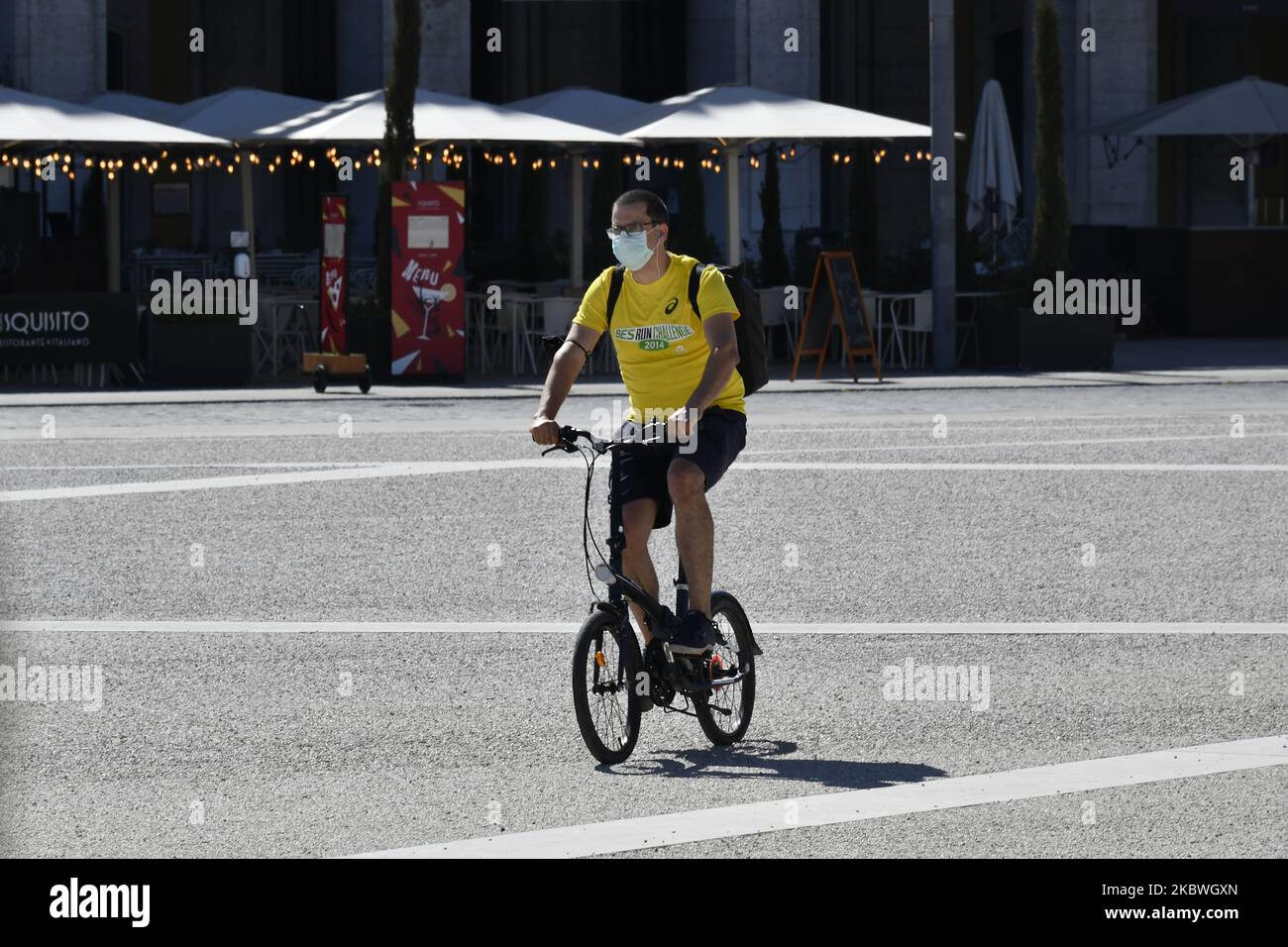 A person wearing a protective mask rides a bicycle through Praça de Comércio, Lisbon. On July 31st, 2020 in Lisbon, Portugal. Health Minister Marta Temido reported that there are 12,864 active cases of COVID-19 disease in Portugal, including outbreak-related infections. In total there are 194 active outbreaks in the country: 47 in the North region, 12 in the Centre, 106 in Lisbon and Tagus Valley, 14 in the Alentejo and 15 in the Algarve region. The outbreaks are considered active even if several days have passed since the last confirmed case. 'We only consider an outbreak to be extinct when 2 Stock Photo