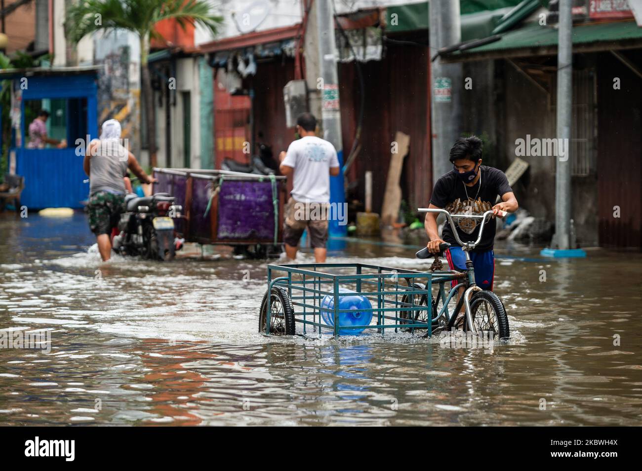 A man with a bicycle sidecar wades through flood water caused by a broken pipe along in Manila, Philippines on July 31, 2020. The country recorded its highest single-day increase of COVID-19 cases on July 31 with 4,063 new cases announced just before the month ended.(Photo by Lisa Marie David/NurPhoto) Stock Photo