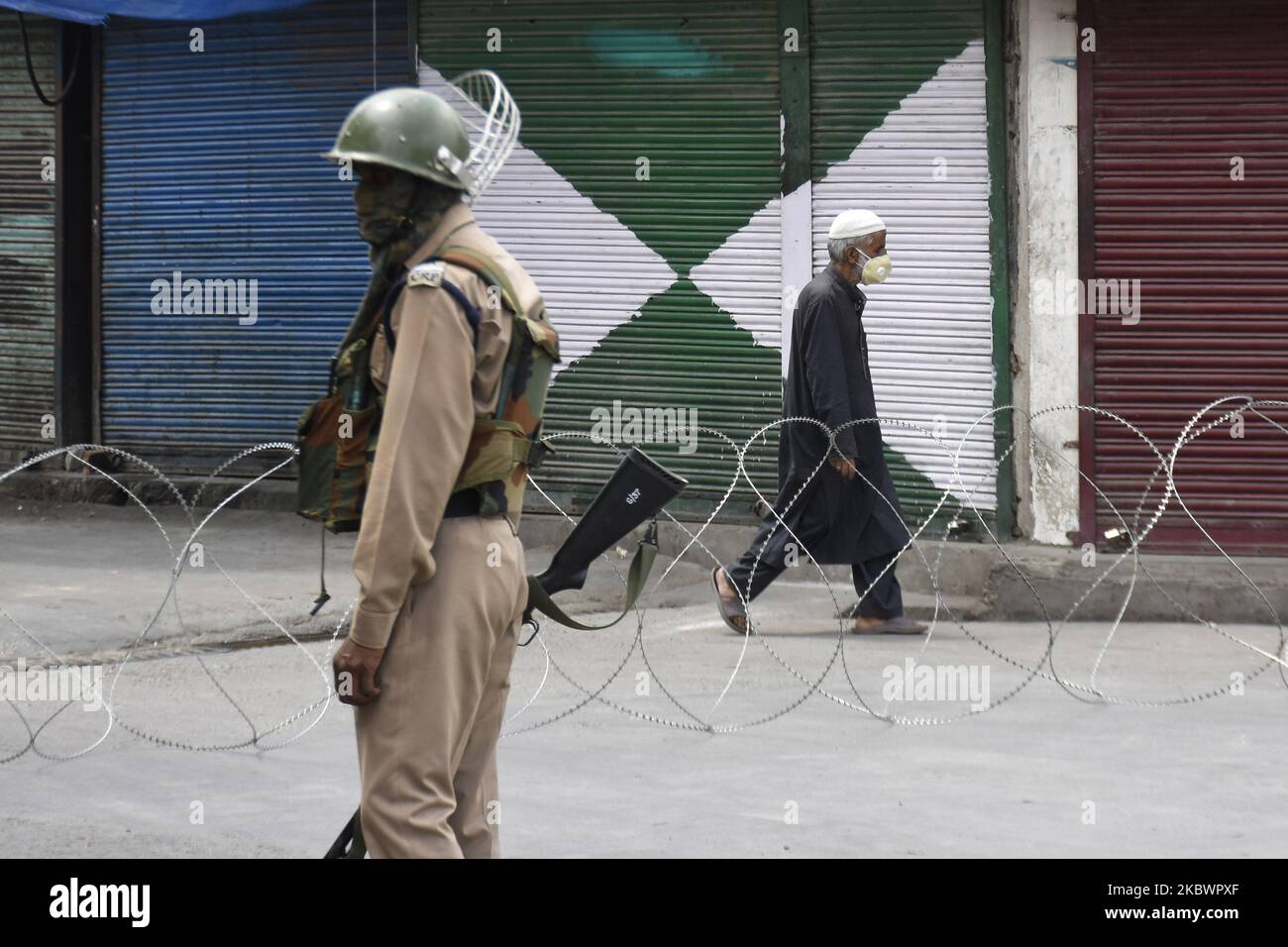 An Indian policeman stands while as Kashmiri man walks besides concertina wire during strict restrictions in Srinagar, Indian Administered Kashmir on 05 August 2020. Restrictions were placed in place on the first anniversary of revocation of Article 370 by Indian government to tackle any protests. (Photo by Muzamil Mattoo/NurPhoto) Stock Photo