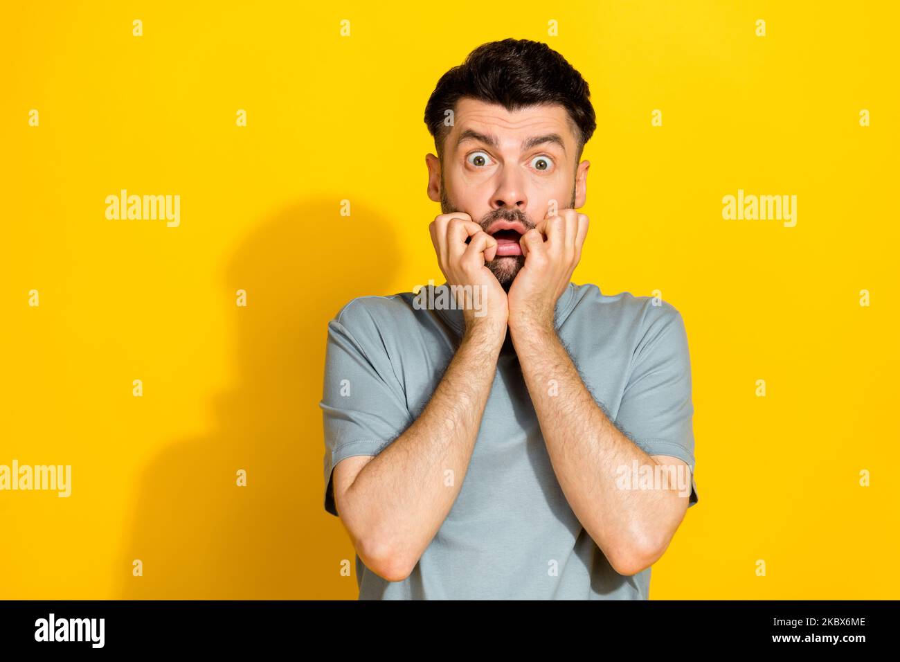 Closeup photo of young excited stressed funny man bearded bite fingers nervous scared watching movie unexpected isolated on yellow color background Stock Photo