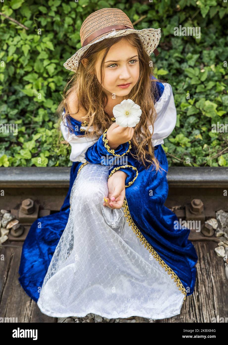 Beautiful girl in blue dress sitting on the rails and holding flower ...