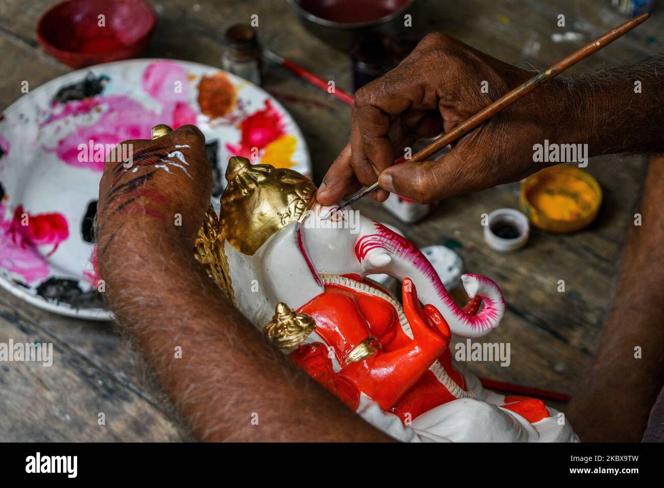 An artisan giving final touches to an idol of Ganesha.Ganesh chaturthi or Ganesh puja is the Hindu festival of celebrating the arrival of Lord Ganesha, the Elephant headed deity of Hindu mythology from Kailash parvaat to earth. People decorate their houses with flowers and ornaments and bring Ganesha idols to worship during this time. This year , the festivities took a hit and showed a decline due to COVID-19 outbreak , forcing peoples into cash crunch. The idol makers and sellers are facing a tough time in the potters hub of Kolkata due to decreased in sales of idols and other stuffs due to C Stock Photo