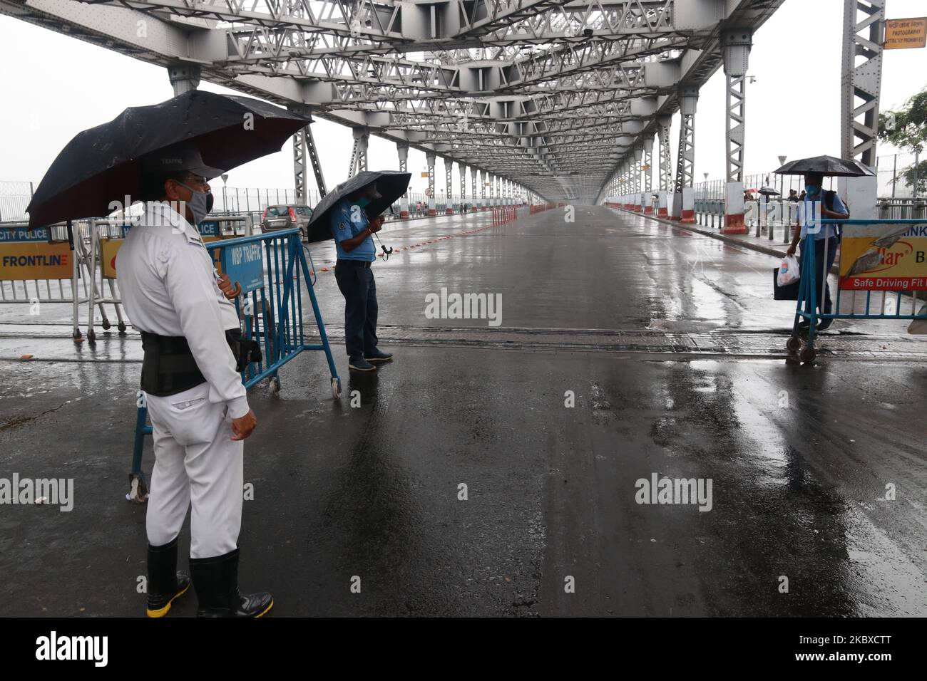 Indian Police carrying umbrellas at the deserted Howrah Bridge on duty  under heavy rain during the second day of the two-day state-imposed  lockdown as a preventive measure against the surge in COVID-19, image size:1300x956