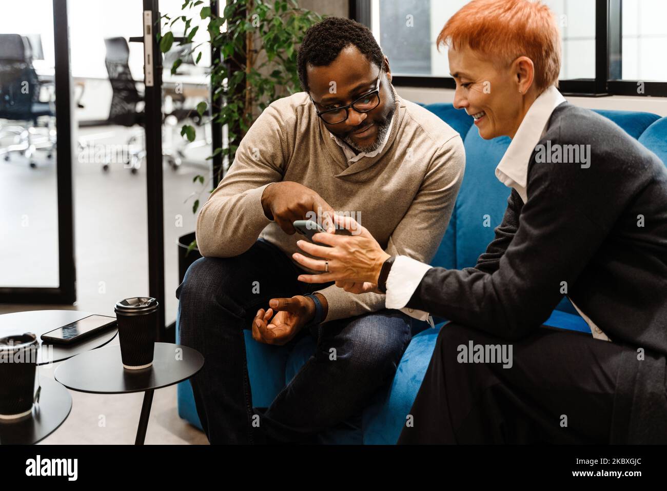 Two multiracial colleagues talking and using cellphone while working in office Stock Photo