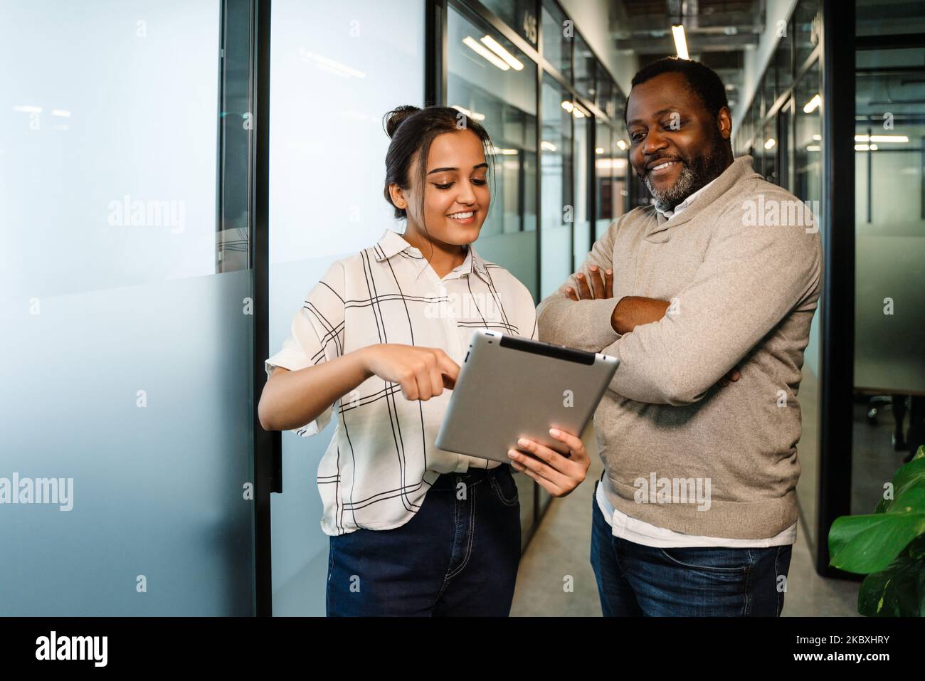 Two multiracial colleagues talking and using tablet computer while working in office Stock Photo