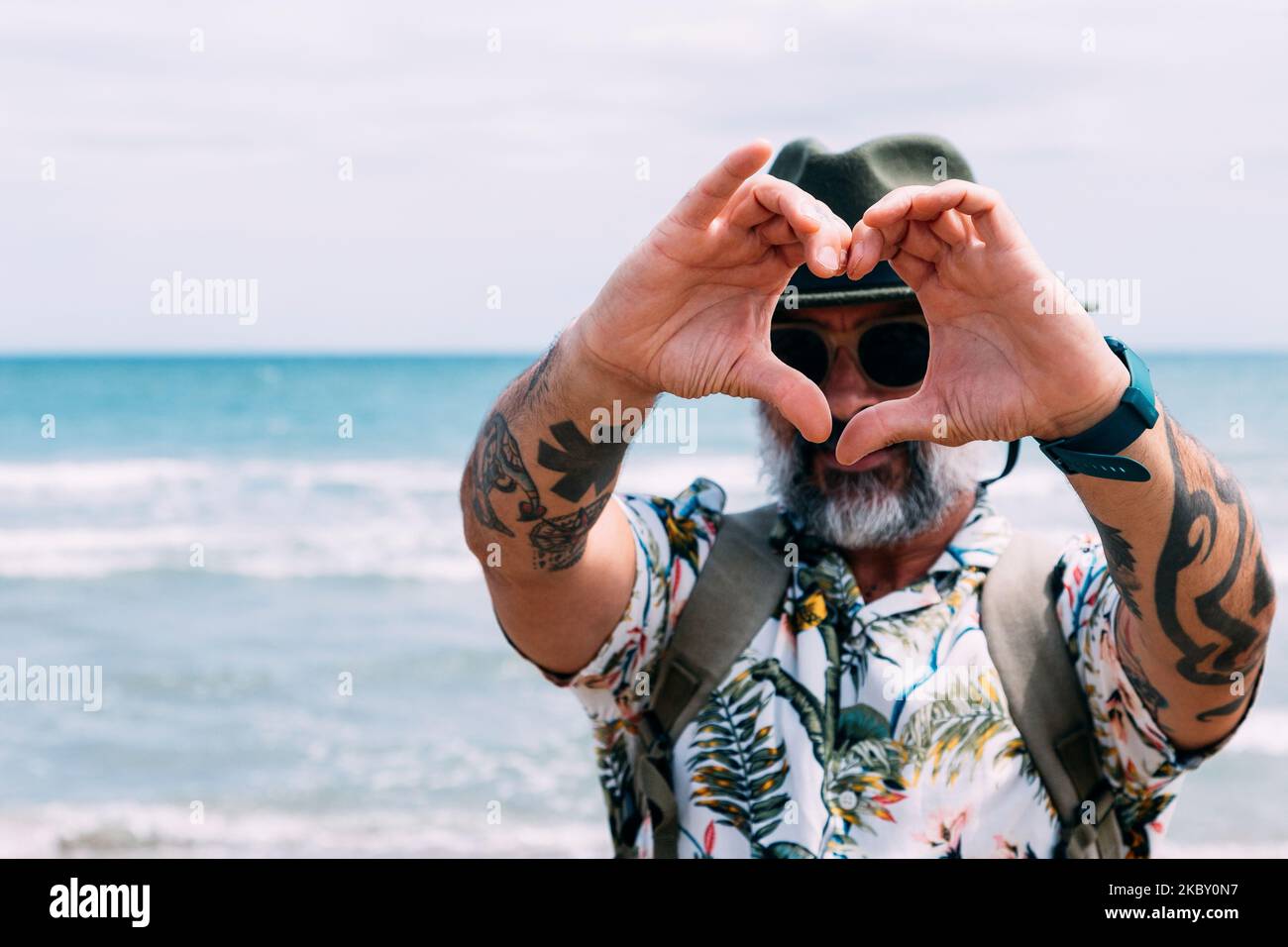 A smiling man making a heart shape with his hands on the beach Stock Photo