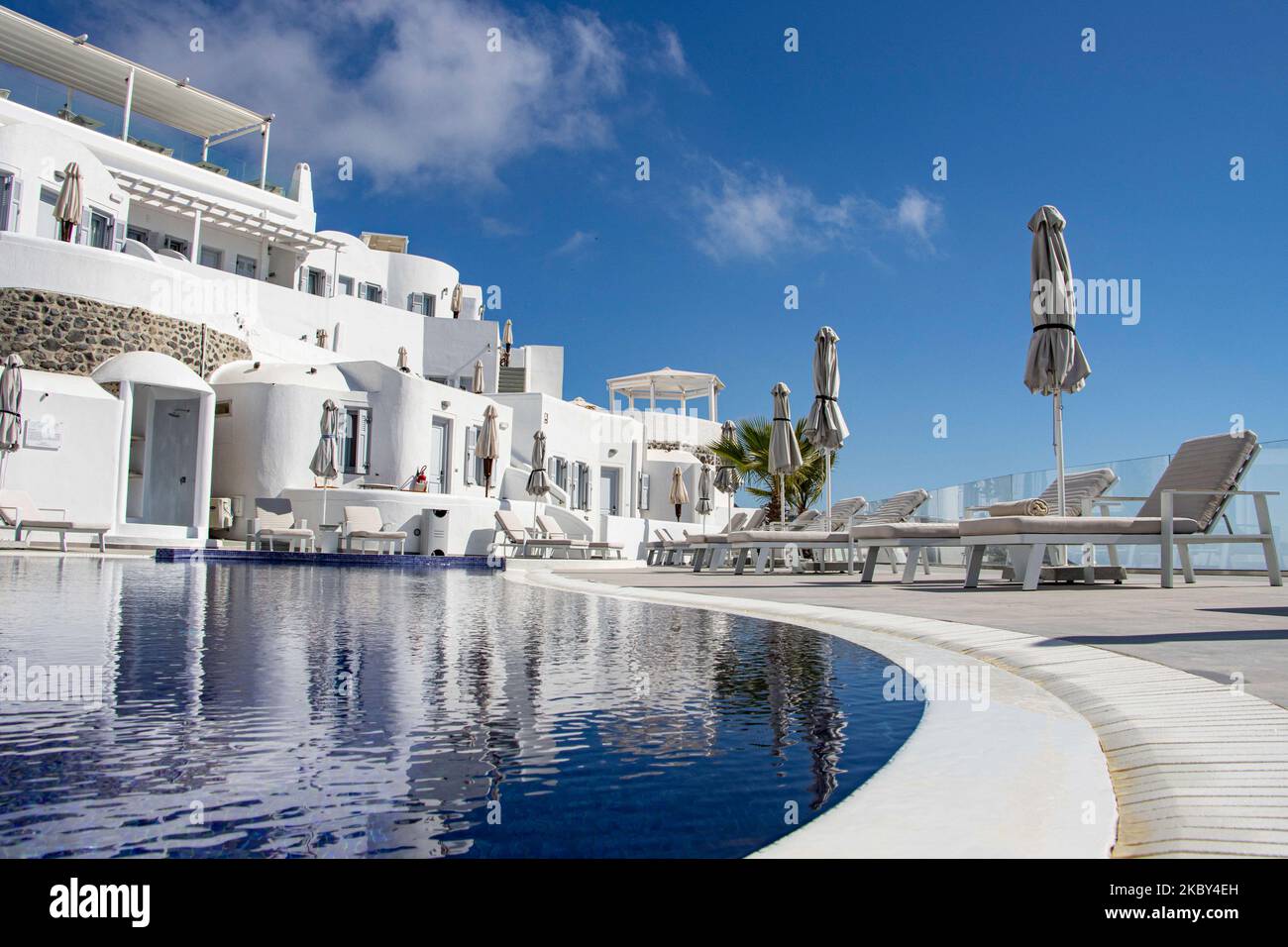 Swimming pool in a 5-star hotel resort with sun deck chairs and towel looking over a beautiful view on the Caldera over the Aegean sea with traditional whitewashed Greek Mediterranean terraced architecture of houses and resorts. Santorini Island in the Cyclades, Greece during a hot sunny summer day. Santorini is usually overcrowded as it is famous for its sunset attracting mostly couples from all over the world for the magical sunset view over the volcano, but this year due to the Coronavirus Covid-19 pandemic there are less than usual arrivals, reducing also the income of the GDP of the count Stock Photo