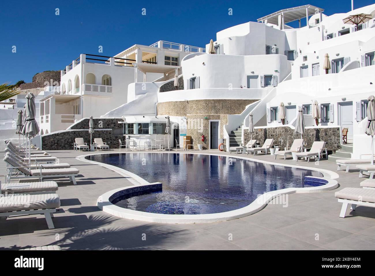 Swimming pool in a 5-star hotel resort with sun deck chairs and towel looking over a beautiful view on the Caldera over the Aegean sea with traditional whitewashed Greek Mediterranean terraced architecture of houses and resorts. Santorini Island in the Cyclades, Greece during a hot sunny summer day. Santorini is usually overcrowded as it is famous for its sunset attracting mostly couples from all over the world for the magical sunset view over the volcano, but this year due to the Coronavirus Covid-19 pandemic there are less than usual arrivals, reducing also the income of the GDP of the count Stock Photo