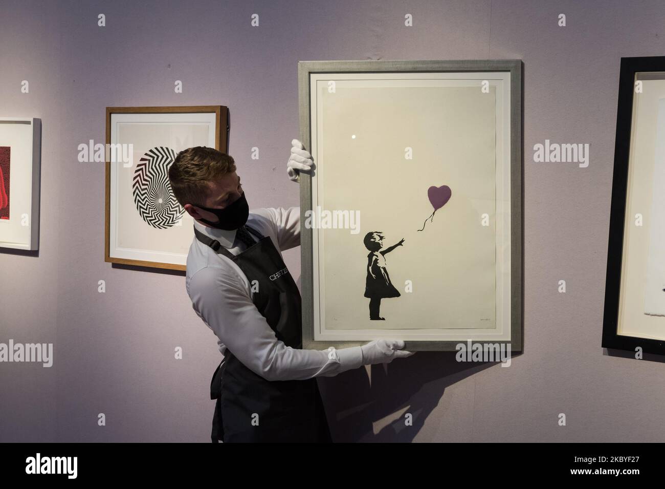 (EDITOR'S NOTE: Editorial use only) A staff member holds 'Girl with Balloon - Colour AP (Purple)' screenprint in colours, 2004, by Banksy (estimated sale price ?250,000-350,000) during a press preview of 'Banksy: I can't believe you morons actually buy this sh*t' online sale at Christie's on September 09, 2020 in London, England. The sale, taking place from 10 - 23 September, is named after Banksy's 2007 screenprint Morons (Sepia), which cheekily references the record-breaking sale of Vincent van Gogh's Sunflowers at Christie's in 1987. (Photo by WIktor Szymanowicz/NurPhoto) Stock Photo