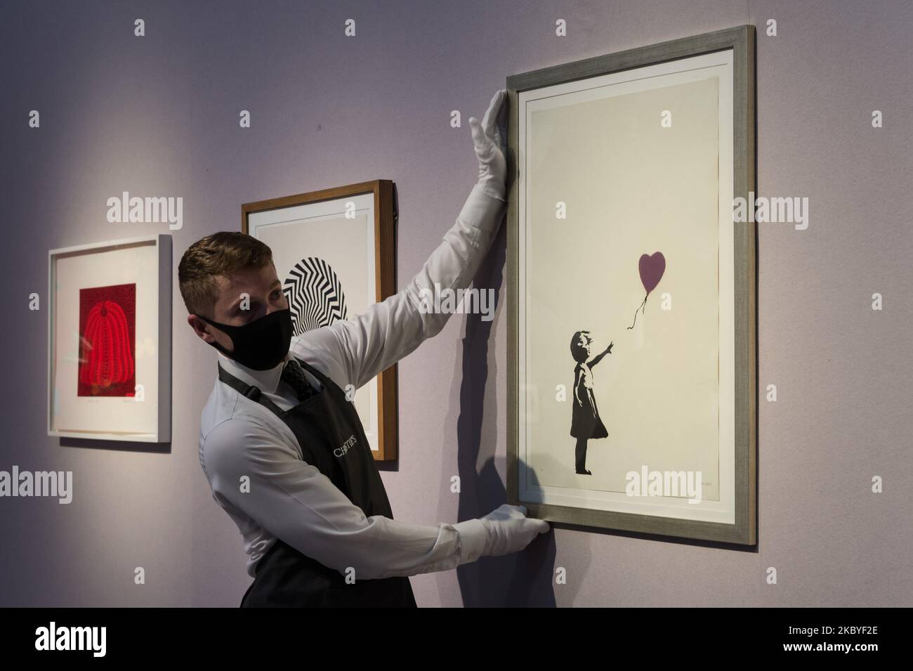 (EDITOR'S NOTE: Editorial use only) A staff member poses with 'Girl with Balloon - Colour AP (Purple)' screenprint in colours, 2004, by Banksy (estimated sale price ?250,000-350,000) during a press preview of 'Banksy: I can't believe you morons actually buy this sh*t' online sale at Christie's on September 09, 2020 in London, England. The sale, taking place from 10 - 23 September, is named after Banksy's 2007 screenprint Morons (Sepia), which cheekily references the record-breaking sale of Vincent van Gogh's Sunflowers at Christie's in 1987. (Photo by WIktor Szymanowicz/NurPhoto) Stock Photo
