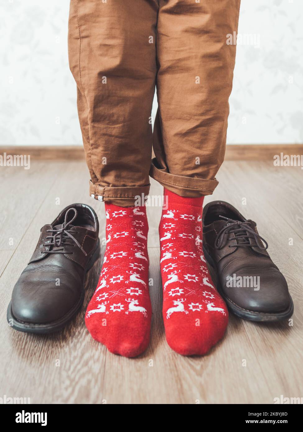 Young man in chinos trousers and bright red socks with reindeers on them is ready to wear suede shoes. Scandinavian pattern. Winter holiday spirit. Stock Photo