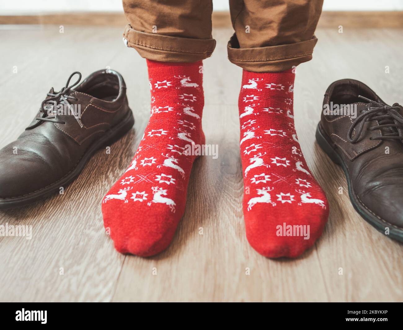 Young man in chinos trousers and bright red socks with reindeers on them is ready to wear suede shoes. Scandinavian pattern. Winter holiday spirit. Stock Photo
