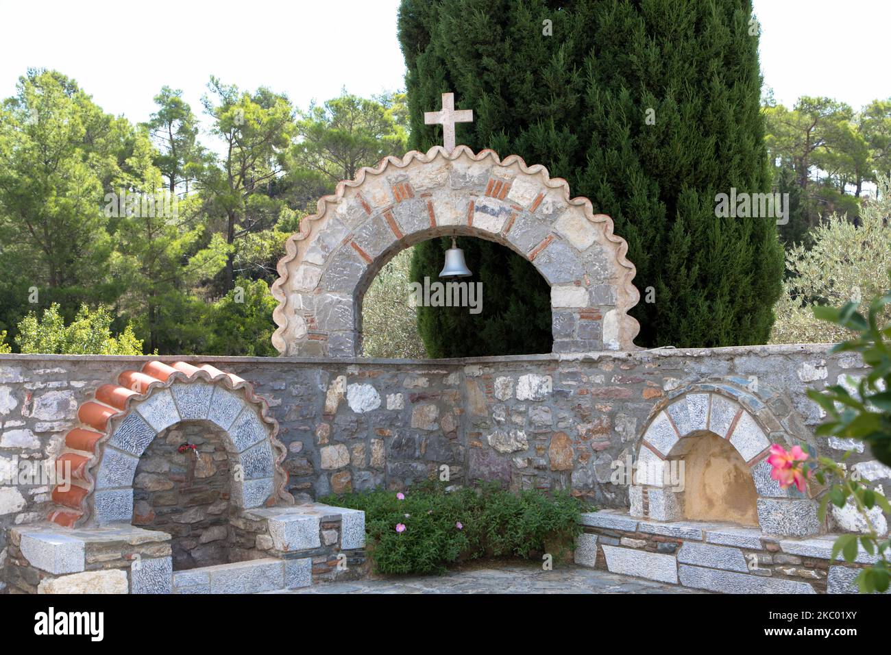 Sandstone arch with bell and religious cross in front of a wild and romantic landscape. Seen at Moni Thari Monastery in Laerma. Rhodes Island Stock Photo
