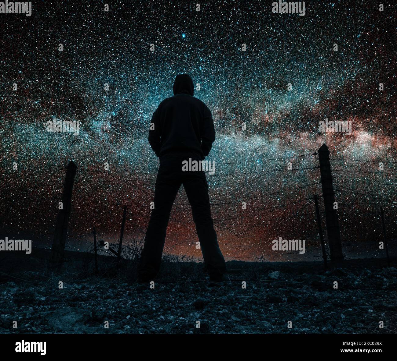 Rear view of man near barbed wire fence stargazing. Dark skies, air pollution... Stock Photo
