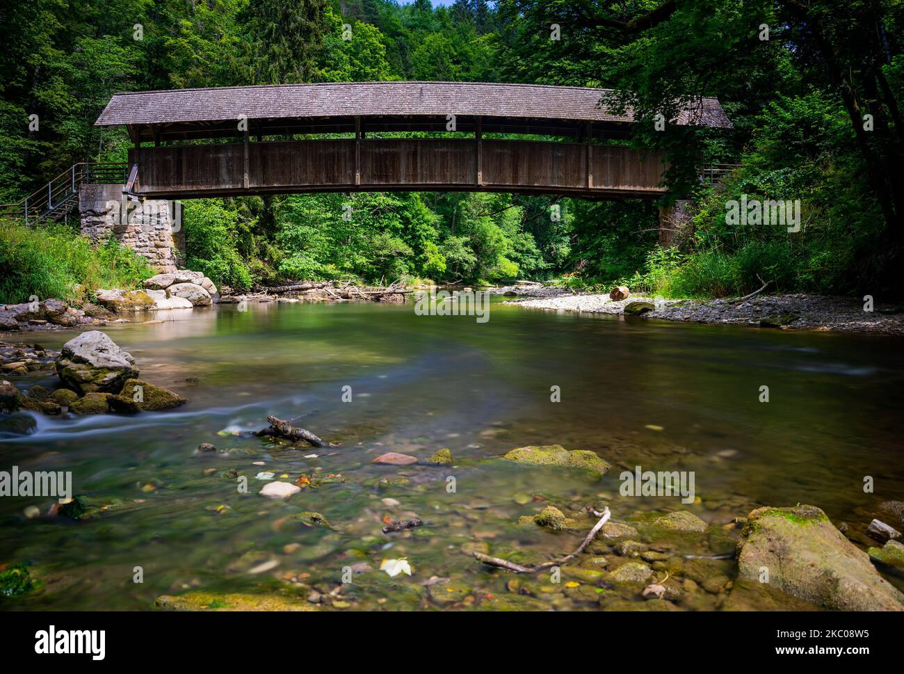 A flowing rocky river surrounded by dense trees and building Stock Photo
