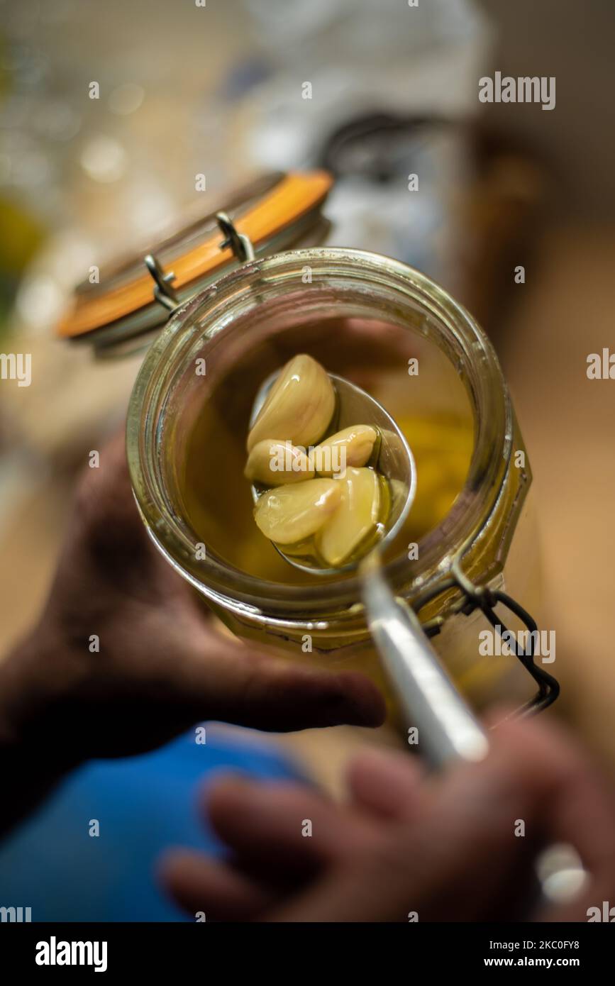 A top view of adult hand using tablespoon to scoop pickled garlic out
