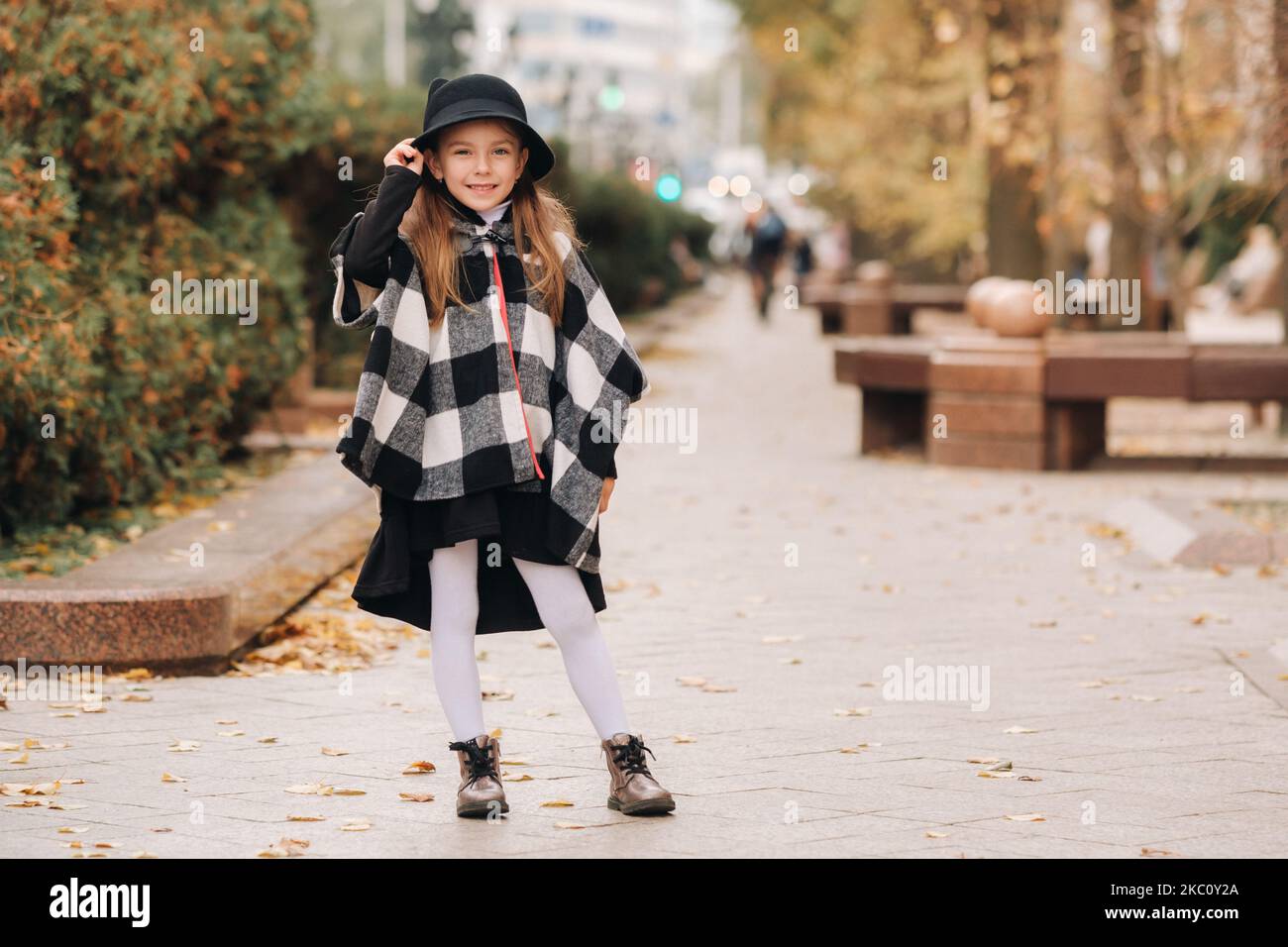 A stylish little girl in a hat walks around the autumn city Stock Photo