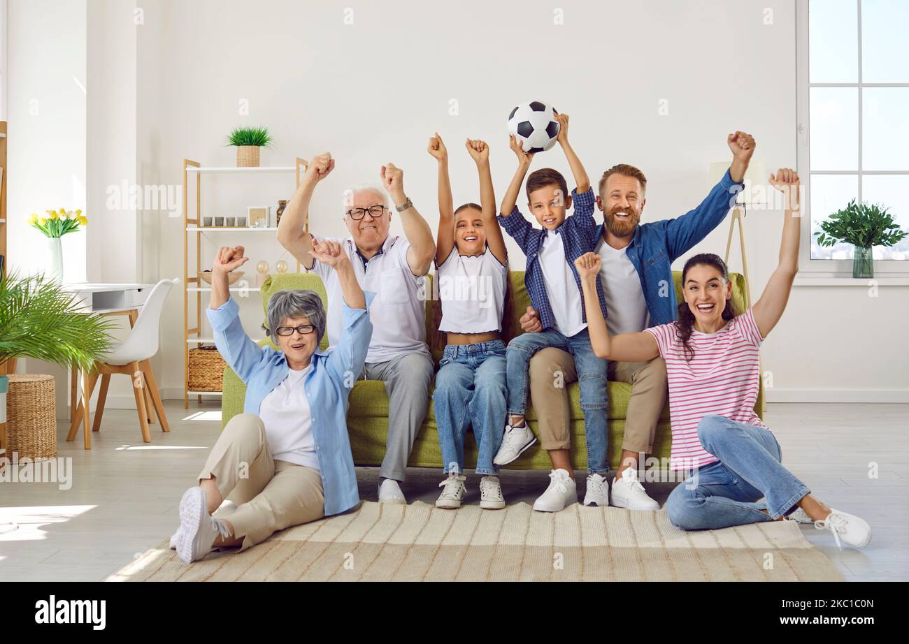 Modern active family of three generations is watching football match on TV at home together. Stock Photo