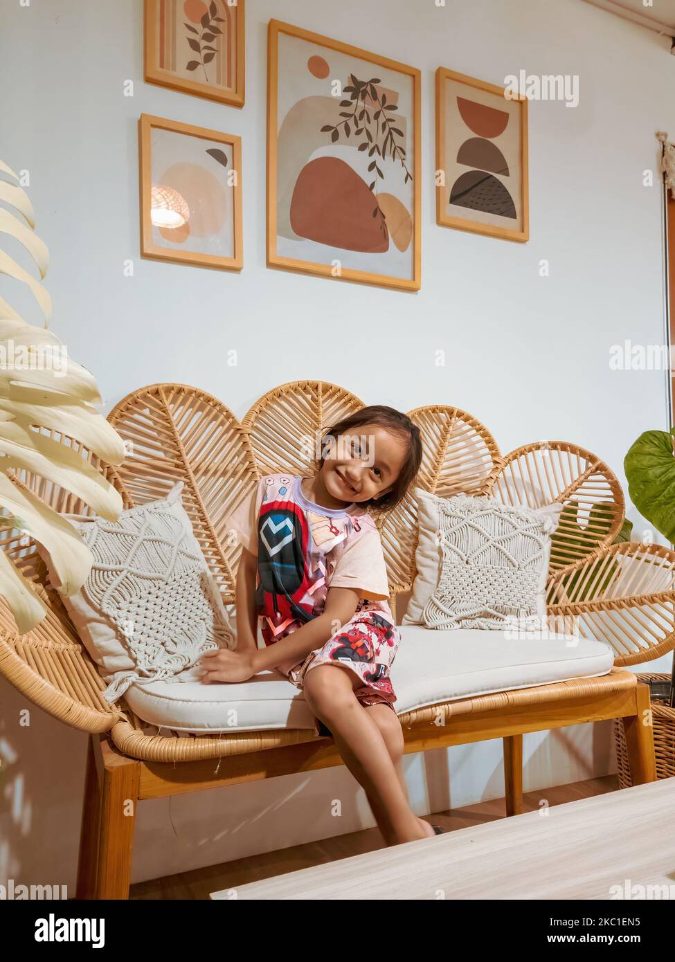 Happy little girl sitting on the rattan couch in a boho interior design ...