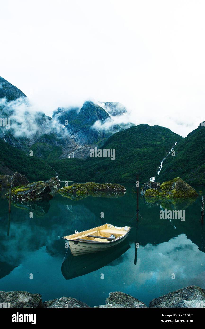 A small wooden boat in a turquoise lake surrounded by clouds-covered ...