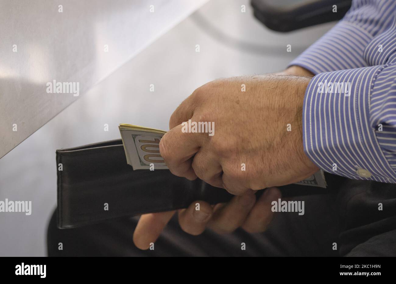 An Iranian man puts the U.S. Dollar banknotes in his wallet as he sits in a currency exchange shop in Tehran’s business district on October 10, 2020. U.S. Dollar has risen again. You may see the price under 300,000 IRR for each Dollar on the electronic board displayed at the currency exchange shops, but the real USD price was 300,000 IRR for buy and 3,250,000 IRR for sale on each Dollar, A street money changer told the photographer. (Photo by Morteza Nikoubazl/NurPhoto) Stock Photo