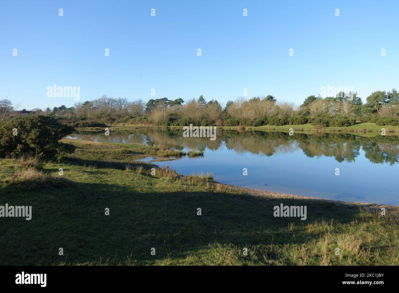 A bright winter day with mirror smooth water suirface on the lakes formed in the nature reserve on the disused airfield at Greenham Common Airbase nea Stock Photo