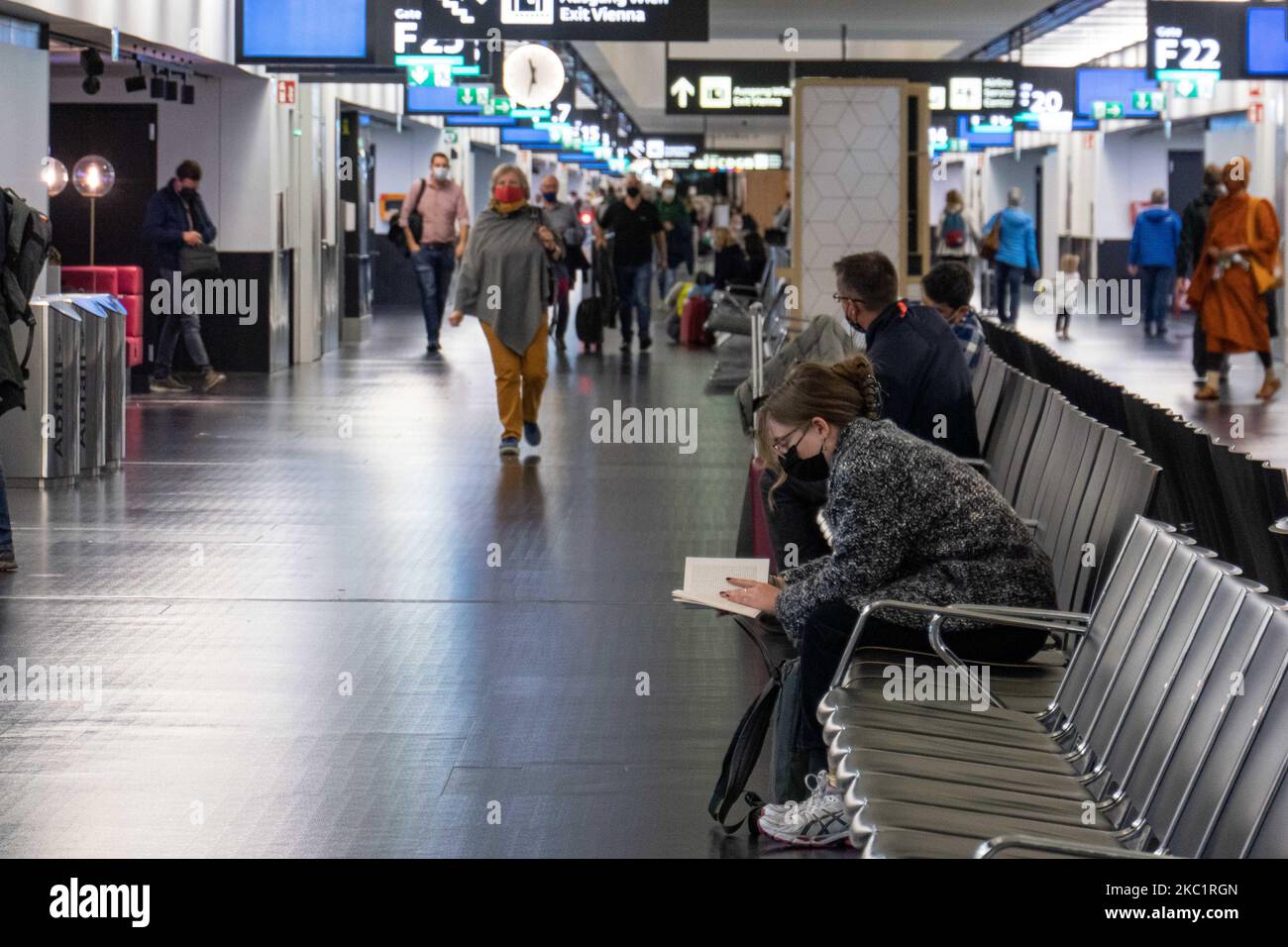 A young woman with a facemask reading a book while she is waiting for her flight. Passengers wearing facemasks, face shields, gloves and other safety measures are seen in the airport terminal, at the F Gates area of Vienna International Airport VIE LOWW - Flughafen Wien-Schwechat serving the Austrian Capital but also Bratislava as it is 55km away from the Slovak city during the Covid-19 Coronavirus pandemic era. There is a second wave coming while cases are increasing, facemask become mandatory, social distancing measures and disinfecting hand sanitizer are everywhere while new lockdowns or mi Stock Photo