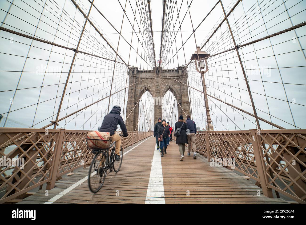 Pedestrians and bicycles on brooklyn bridge. The Brooklyn Bridge in New York City in the United States as seen during a cloudy day with tourists and locals on it. The famous bridge, a landmark for NYC and the United States of America is a hybrid cable stayed suspension bridge spanning the East River between the boroughs of Manhattan and Brooklyn. The historical NY landmark bridge was built between 1869 and 1883. New York, USA on February 13, 2020 (Photo by Nicolas Economou/NurPhoto) Stock Photo