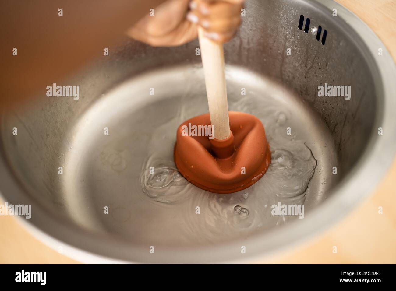 Side View Of A Female Plumber Using Plunger In Kitchen Sink Stock Photo