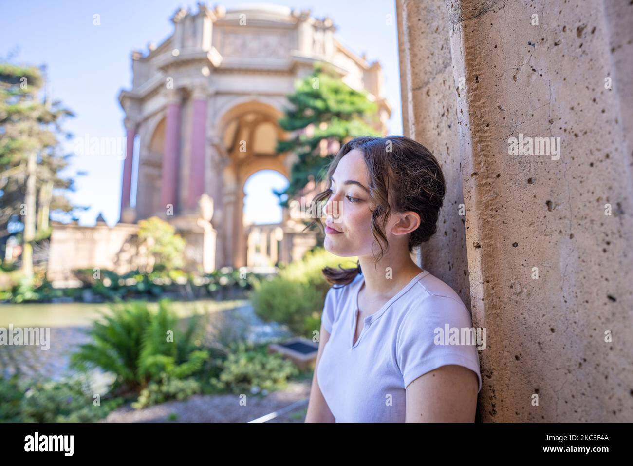 Wide Angle Portrait of Teenage Female Leaning Against a Roman Column with the Palace of Fine Art in the Background Stock Photo