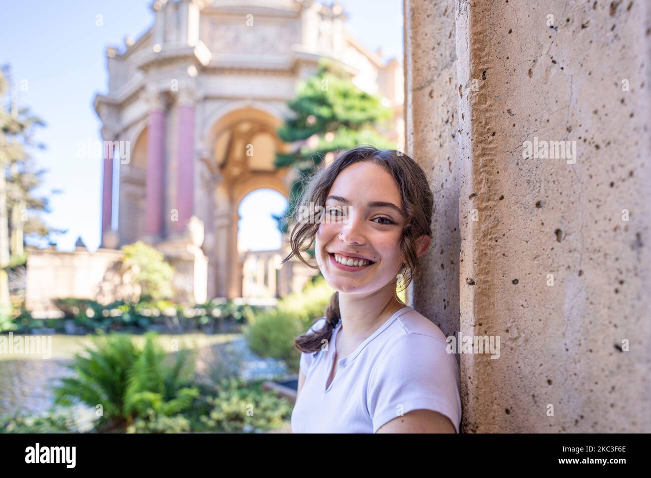 Wide Angle Portrait of Teenage Female Leaning Against a Roman Column with the Palace of Fine Art in the Background Stock Photo